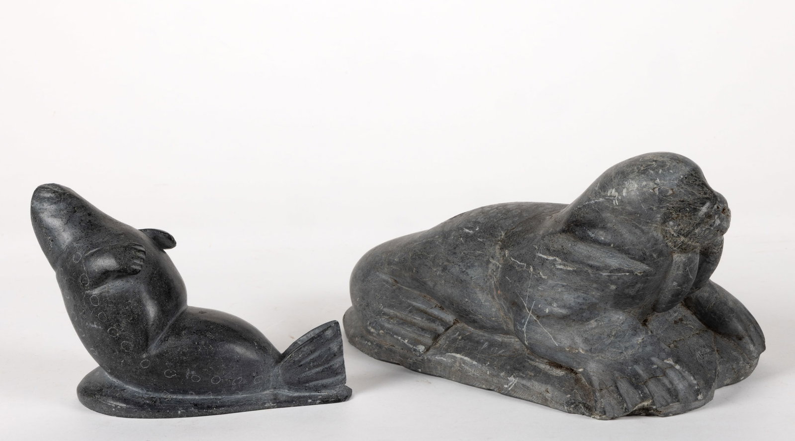 CANADIAN INUIT CARVED SOAPSTONE ANIMAL FIGURES, LOT OF TWO: CANADIAN INUIT CARVED SOAPSTONE ANIMAL FIGURES, LOT OF TWO, depicting a walrus with textured snout, prominent carved tusks and detailed flippers resting on an integral stone base, and a reclining