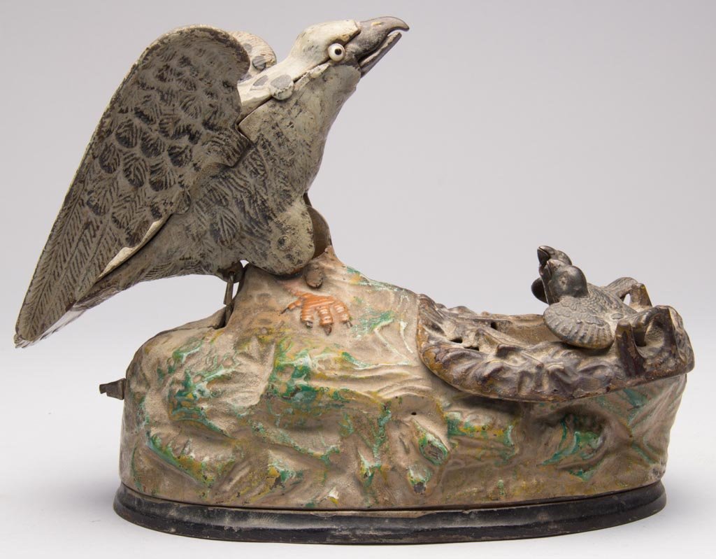 EAGLE AND EAGLETS CAST-IRON MECHANICAL BANK: EAGLE AND EAGLETS CAST-IRON MECHANICAL BANK, patent information under base, original glass eyes, coin trap cover and paint. J. & E. Stevens & Co. Fourth quarter 19th century. 5 3/4" H. Provenance: Fro