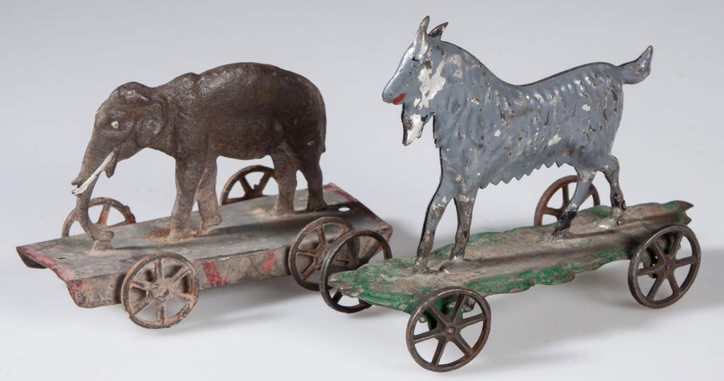 ASSORTED ANIMAL ON PLATFORM PULL TOYS, LOT OF TWO: ASSORTED ANIMAL ON PLATFORM PULL TOYS, LOT OF TWO, comprising a pressed tin goat and a cast-iron elephant, each with cast-iron wheels. Second half 19th century. 4 1/2" and 3 3/4" L. Provenance: The es