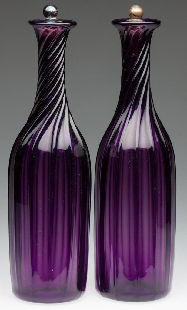 SWIRLED PILLAR-MOLDED PAIR OF DECANTERS: SWIRLED PILLAR-MOLDED PAIR OF DECANTERS, deep brilliant amethyst, each of cylinder form with 12 ribs swirled to the right on the tapered neck, a plain, flared mouth, and polished pontil mark. Necks no