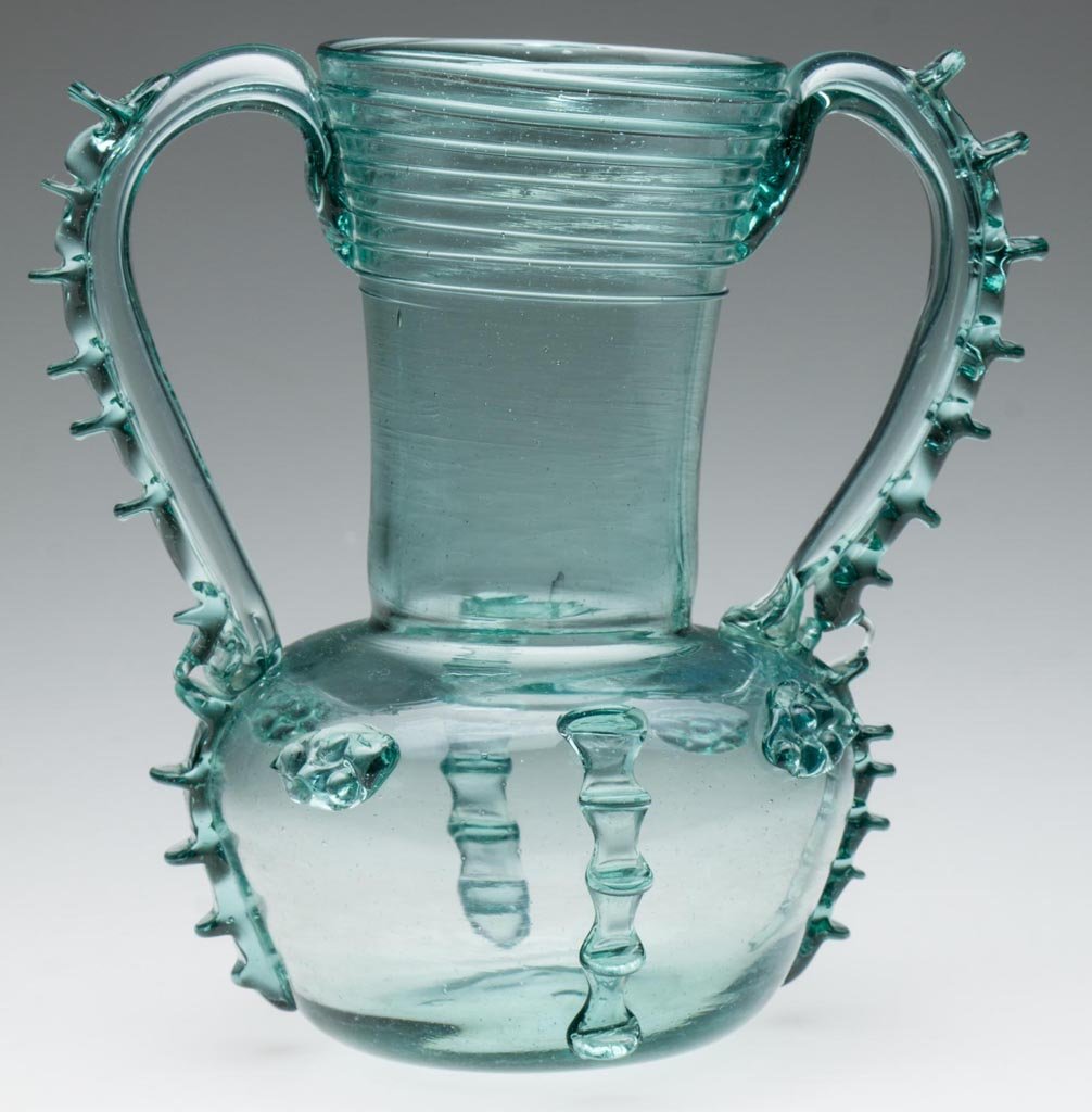 DECORATED FREE-BLOWN VASE: DECORATED FREE-BLOWN VASE, blue green bottle glass, two applied hollow handles with rigaree, additional applied rigaree, prunts and threading, four-prong pontil mark under base. 19th or 20th century. 