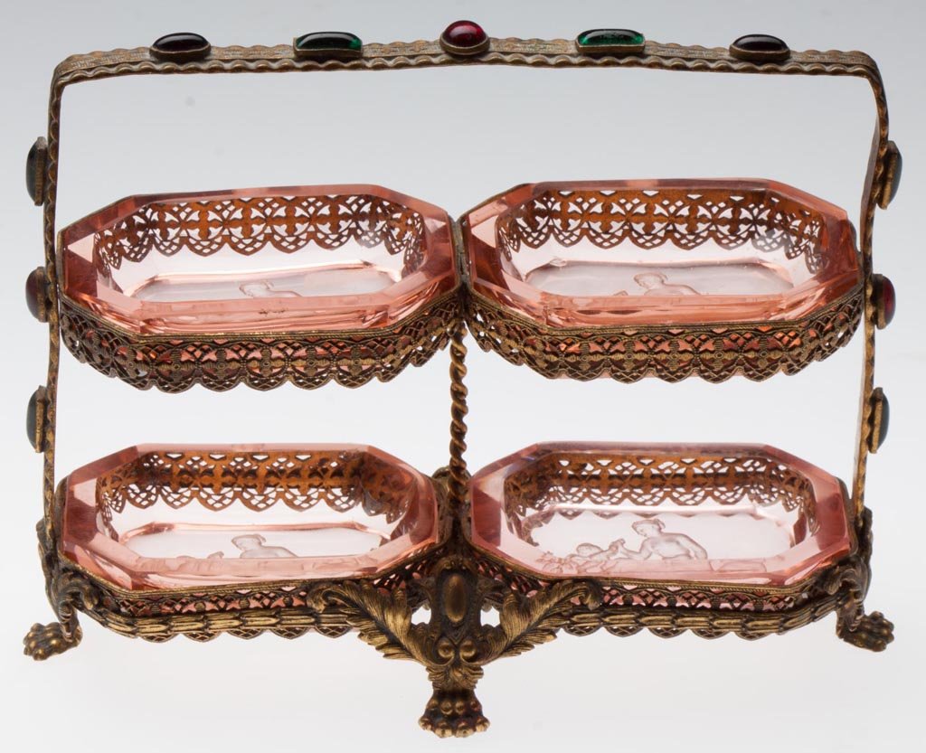 INTAGLIO GLASS OPEN SALTS, SET OF FOUR: INTAGLIO GLASS OPEN SALTS, SET OF FOUR, pink, fitted in a two-tier gilt-metal stand set with jewels. Probably Czechoslovakia. First half 20th century. 4" HOA, 5 1/2" WOA. Provenance: From a North Caro