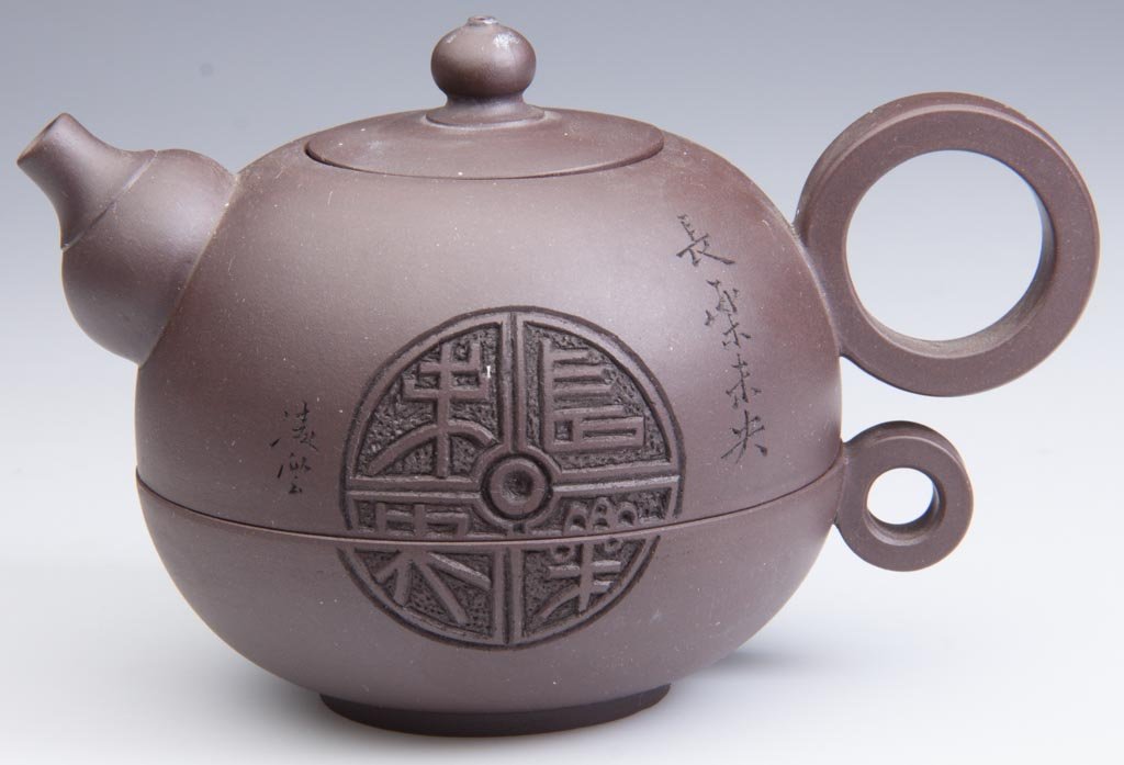 CHINESE YIXING ZISHA CLAY ARTISTIC DARK-BROWN TEAPOT AN: CHINESE YIXING ZISHA CLAY ARTISTIC DARK-BROWN TEAPOT AND COVER, the nested teapot formed as a two-part globe, the bottom half forming the cup, with an applied ring handle, the upper half forming the t