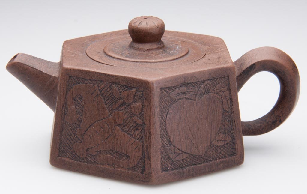 CHINESE YIXING ZISHA CLAY ARTISTIC BROWN TEAPOT AND COV: CHINESE YIXING ZISHA CLAY ARTISTIC BROWN TEAPOT AND COVER, the body of paneled hexagonal form, with paneled spout and handle, the round cover with button-form knop, the teapot sides incised with an ap
