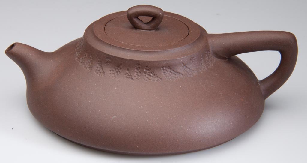 CHINESE YIXING ZISHA CLAY ARTISTIC BROWN TEAPOT AND COV: CHINESE YIXING ZISHA CLAY ARTISTIC BROWN TEAPOT AND COVER, the body of swelling cylindrical form, with tube-form handle and spout, the round cover with triangular tube knop, the surface completely pla