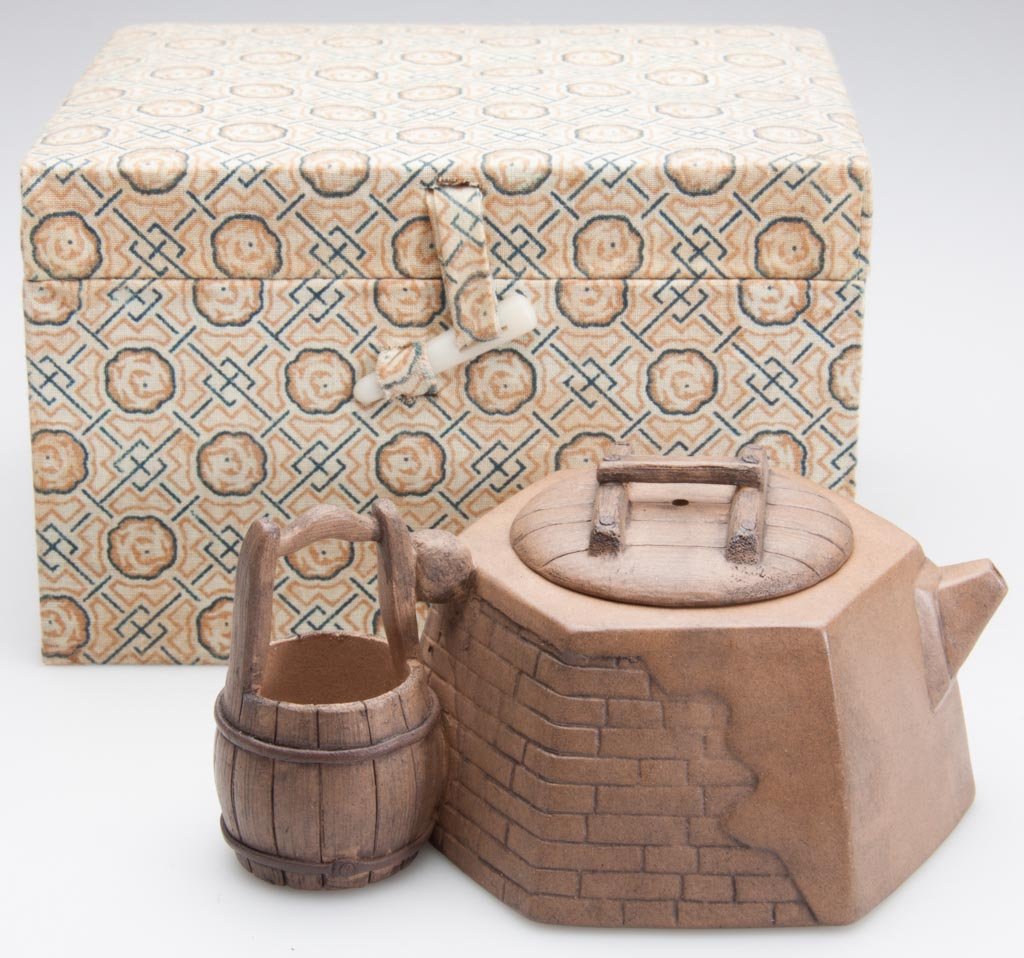 CHINESE YIXING ZISHA CLAY ARTISTIC LIGHT-BROWN TEAPOT A: CHINESE YIXING ZISHA CLAY ARTISTIC LIGHT-BROWN TEAPOT AND COVER, in the shape of a hexagonal trompe l'oeil well made of stone, with a bucket on a wood handle to its side, the cover formed as a barrel 