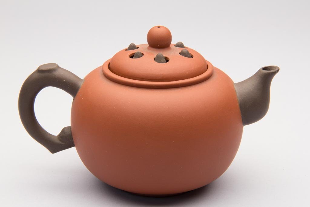CHINESE YIXING ZISHA CLAY ARTISTIC RED TEAPOT AND COVER: CHINESE YIXING ZISHA CLAY ARTISTIC RED TEAPOT AND COVER, of globular form, with dark-brown root-form handle and spout, the domed cover with bead-form knop, the cover with perforations for the brown ce