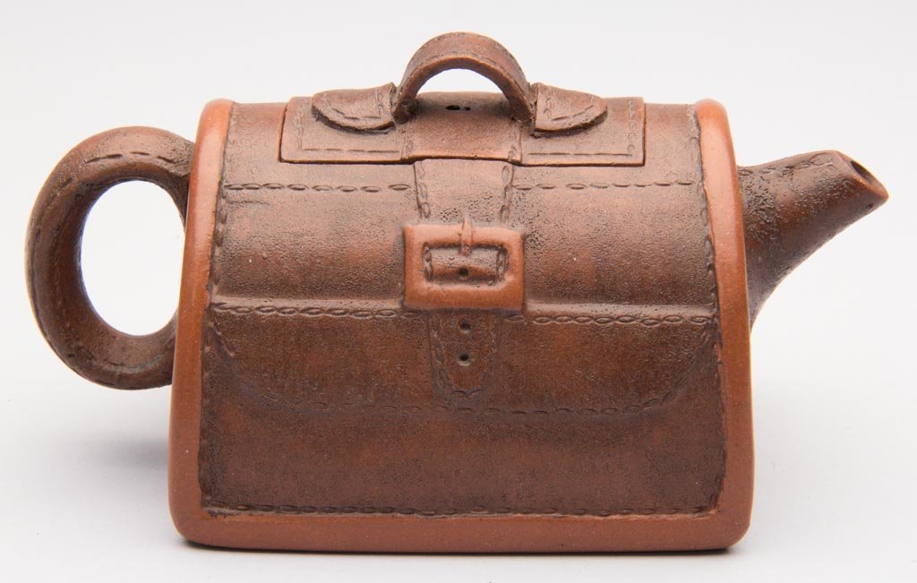 CHINESE YIXING ZISHA CLAY ARTISTIC TEAPOT AND COVER, AT: CHINESE YIXING ZISHA CLAY ARTISTIC TEAPOT AND COVER, ATTRIBUTED TO ZHOU DINGFAN OR XU RUIPING, formed as a trompe l'oeil satchel with strap-form handle and spout, decorated with faux stitching at the 