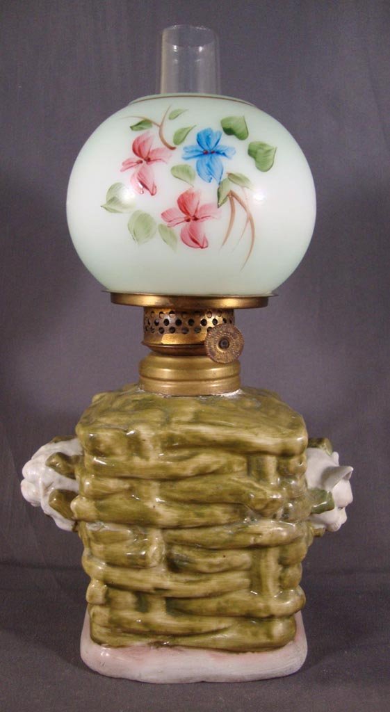 PORCELAIN FIGURAL MINIATURE LAMP: PORCELAIN FIGURAL MINIATURE LAMP, fired décor in green, tan and white, base is a woven basket with a cat and dog head protruding from each end, underside of base is marked PS over an L 5701, opaque w