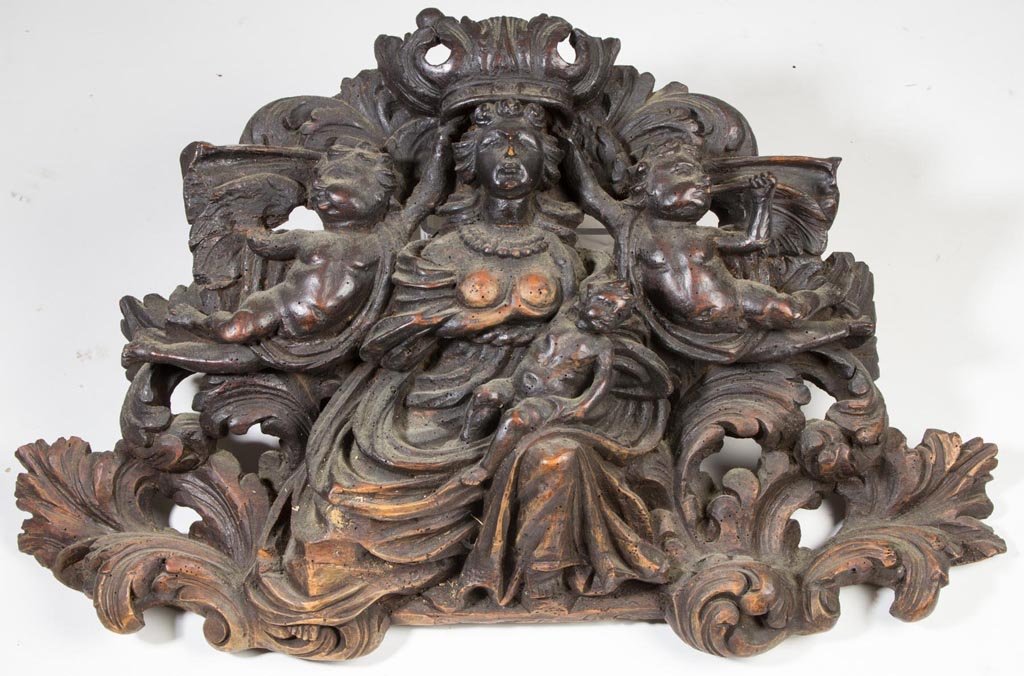 EUROPEAN CARVED WOODEN PLAQUE: EUROPEAN CARVED WOODEN PLAQUE, possibly depicting the Virgin Mary with infant Jesus flanked by cherubs and backed by scrolled elements. Late 19th century. 17" x 27" object size. Provenance: Collection