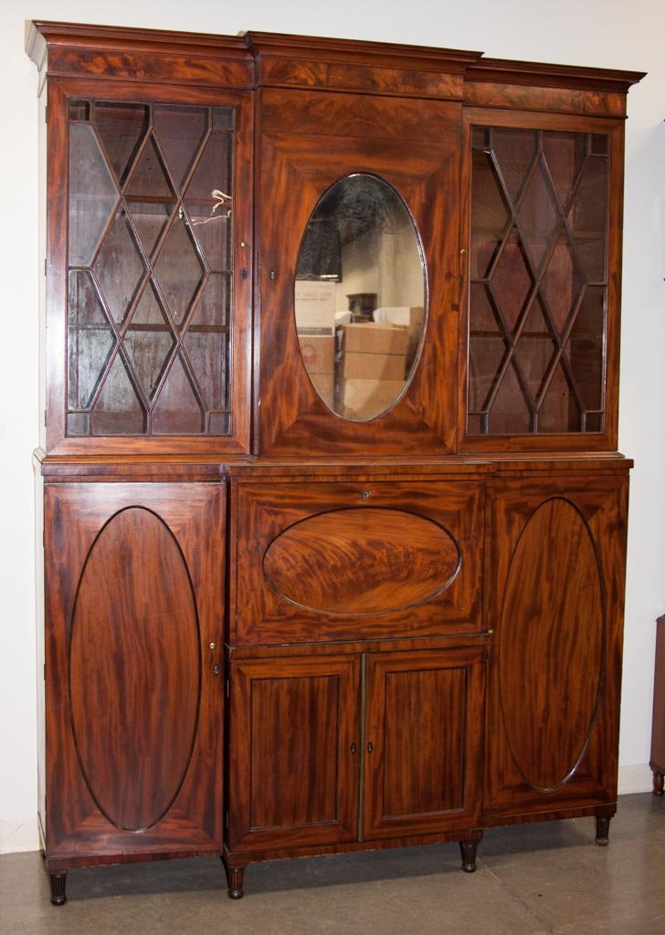 PHILADELPHIA, PENNSYLVANIA SHERATON MAHOGANY BREAKFRONT: PHILADELPHIA, PENNSYLVANIA SHERATON MAHOGANY BREAKFRONT DESK AND BOOKCASE, in three sections, the removable, cove-molded cornice capping two glazed bookcase doors flanking a central cabinet set with a