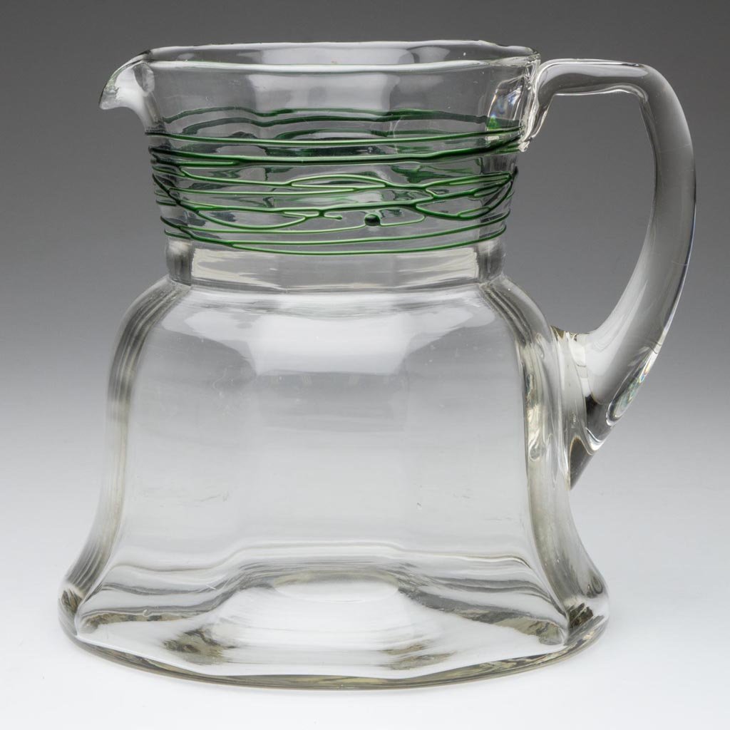 STEUBEN-STYLE THREAD-DECORATED WATER PITCHER: STEUBEN-STYLE THREAD-DECORATED WATER PITCHER, colorless with applied green random threading on neck, bell-form rib-optic body with applied handle and polished pontil mark. First half 20th century. 7 1