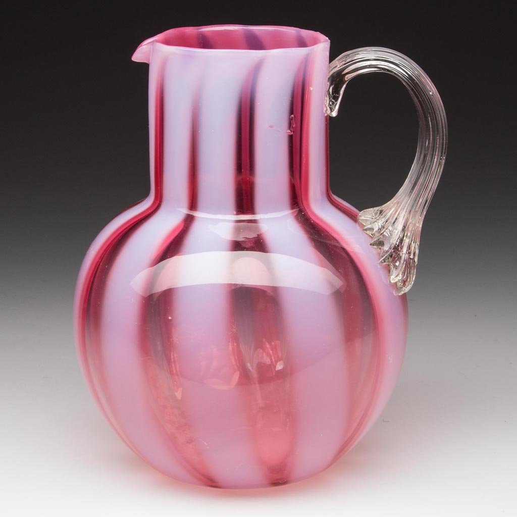 PHOENIX STRIPE-OPTIC CREAMER: PHOENIX STRIPE-OPTIC CREAMER, cranberry opalescent, ball-form with circular rim, colorless applied reeded handle, polished pontil mark. Phoenix Glass Co. 1880 - 1894. 5 1/2" H. Literature: Parallels M