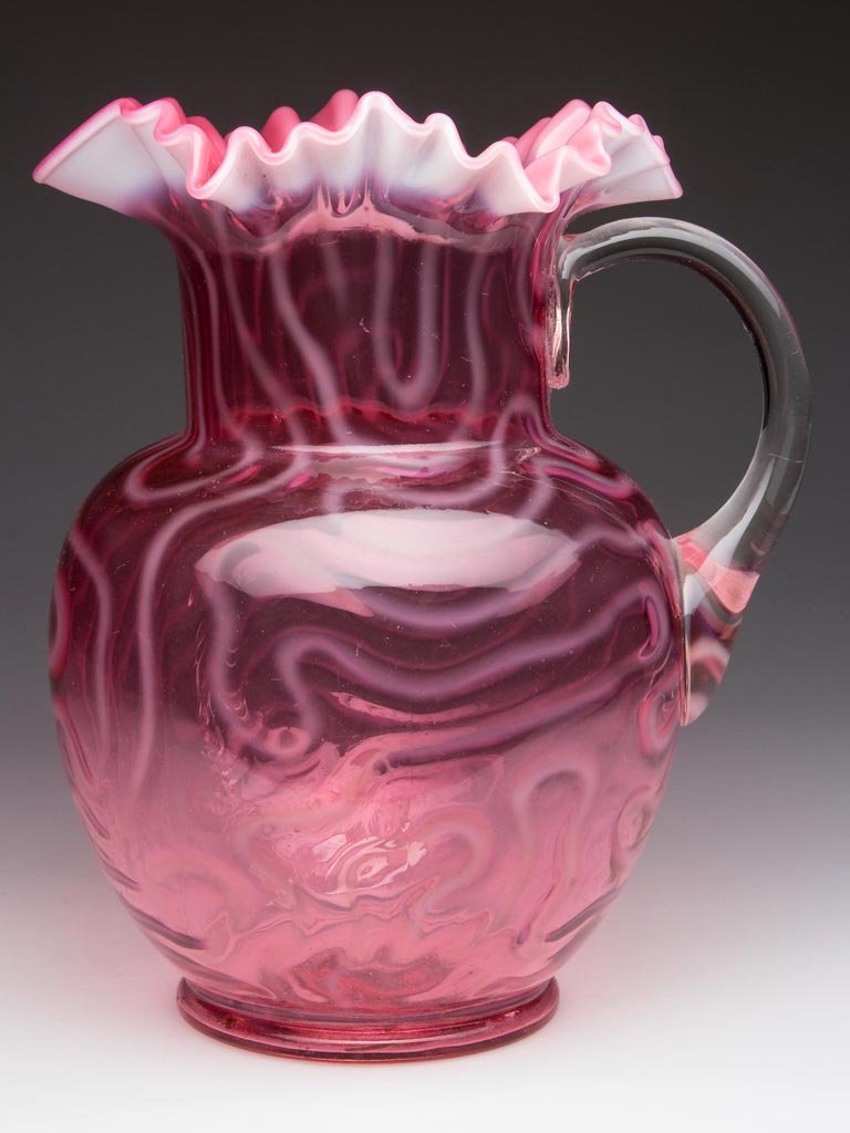 SWIRLING MAZE WATER PITCHER: SWIRLING MAZE WATER PITCHER, cranberry opalescent, bulbous form with star-crimped rim, colorless, applied handle. Attributed to the Jefferson Glass Co. Circa 1905. 9 1/2" H. Literature: Pattern as Hea