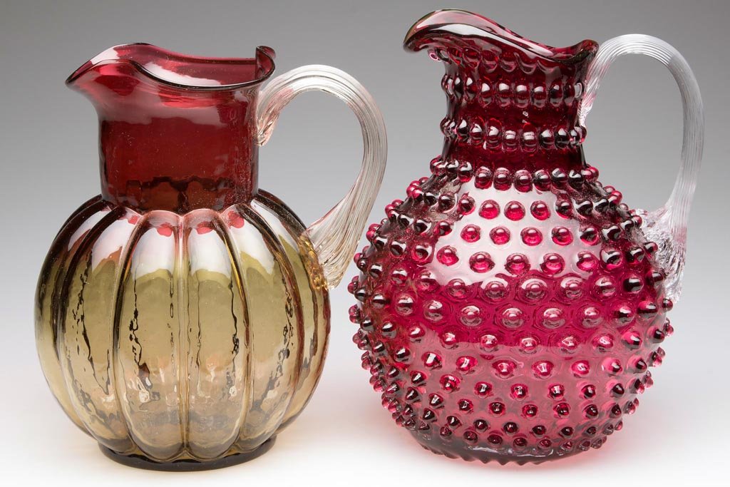 ASSORTED VICTORIAN WATER PITCHERS, LOT OF TWO: ASSORTED VICTORIAN WATER PITCHERS, LOT OF TWO, comprising a deep ruby/cranberry Hobnail example with applied colorless reeded handle and polished pontil mark, and an amberina Melon-Rib example with ap