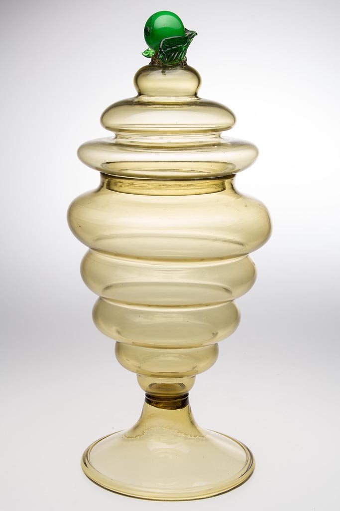 STEUBEN STYLE COVERED URN / VASE: STEUBEN STYLE COVERED URN / VASE, topaz, cover with green apple-form finial, vase raised on a funnel foot with rough pontil mark. First half 20th century. 16 1/2" HOA, 6 1/2" D foot. Provenance: Colle