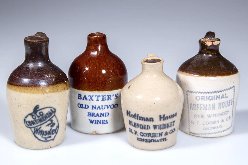 LIQUOR ADVERTISING STONEWARE MOTTO JUGS, LOT OF FOUR: LIQUOR ADVERTISING STONEWARE MOTTO JUGS, LOT OF FOUR, comprising two Hoffman House whiskey, Old Centennial whisky, and Baxter's wines. First quarter 20th century. 2 1/2" to 3 1/4" H. Provenance: From