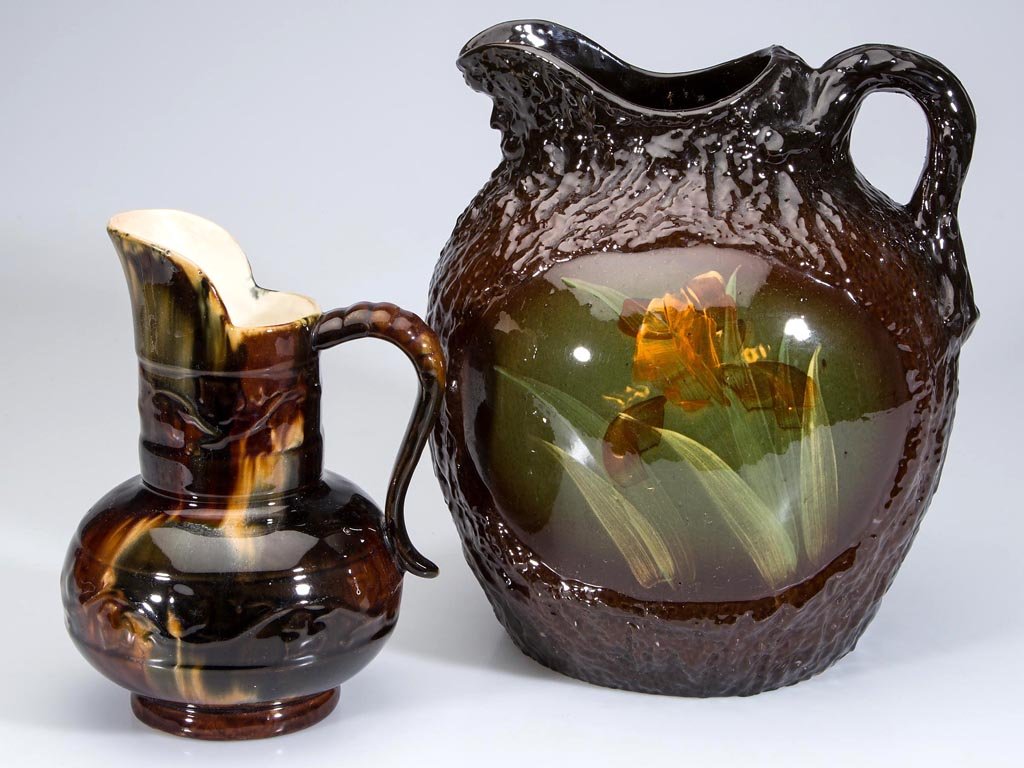 ART POTTERY PITCHERS, LOT OF TWO: ART POTTERY PITCHERS, LOT OF TWO, comprising a large globular-form textured tree pattern brown-glazed yellowware example with molded face to underside of spout, each side with an unpatterned ovoid-for