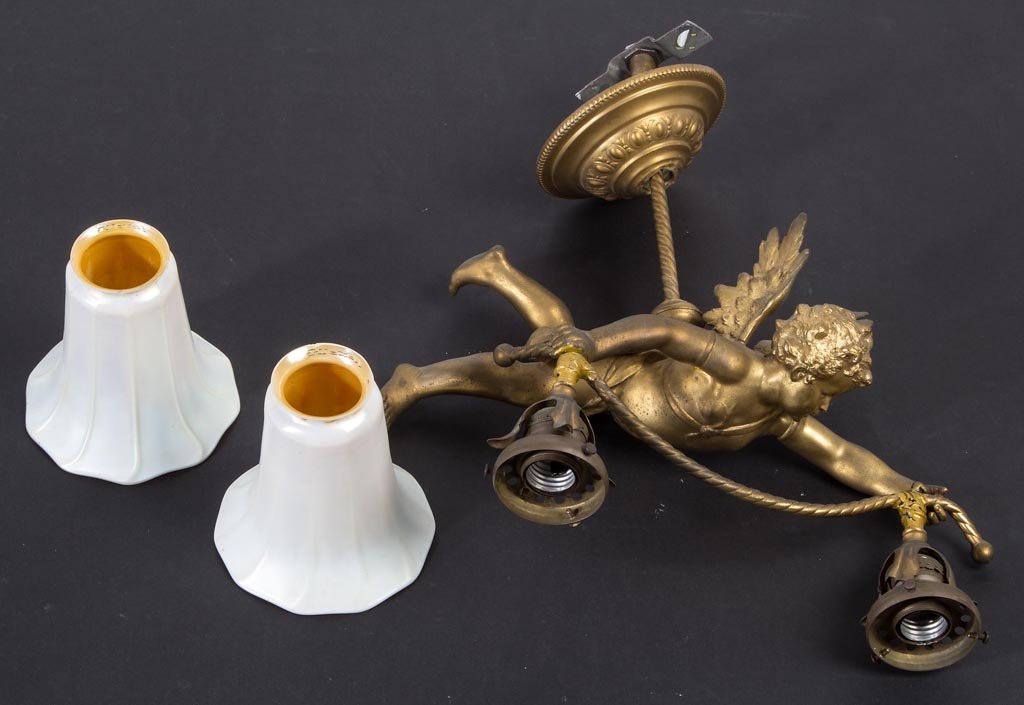 VICTORIAN GILDED SPELTER FIGURAL LIGHT FIXTURE: VICTORIAN GILDED SPELTER FIGURAL LIGHT FIXTURE, depicting a winged cherub holding two electric sockets, supported on a twisted rod and ceiling mount, fitted with two Quezal white and gold luster patte