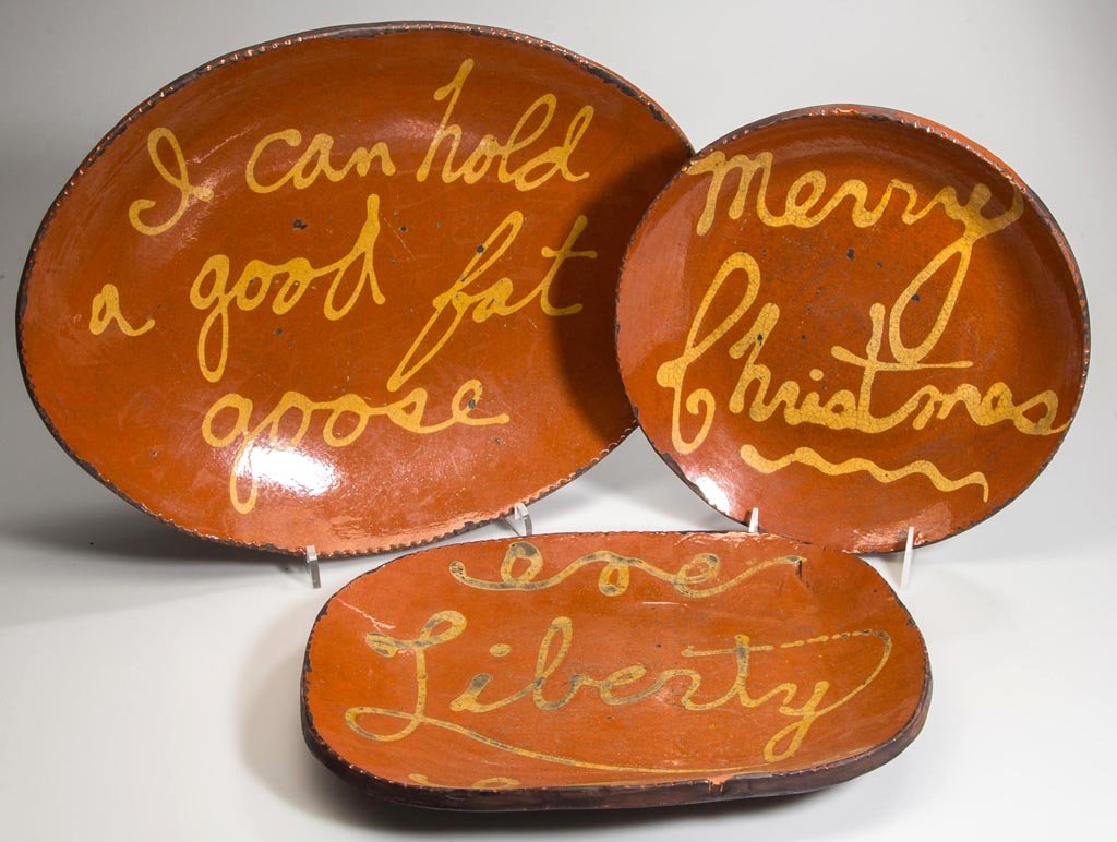 GREG SHOONER REPRODUCTION EARTHENWARE / REDWARE TABLE: GREG SHOONER REPRODUCTION EARTHENWARE / REDWARE TABLE ARTICLES, LOT OF THREE, lead-glazed with slip-trailed inscriptions, comprising an oval "Goose" platter, an oblong "Liberty" platter, and a "Merry 