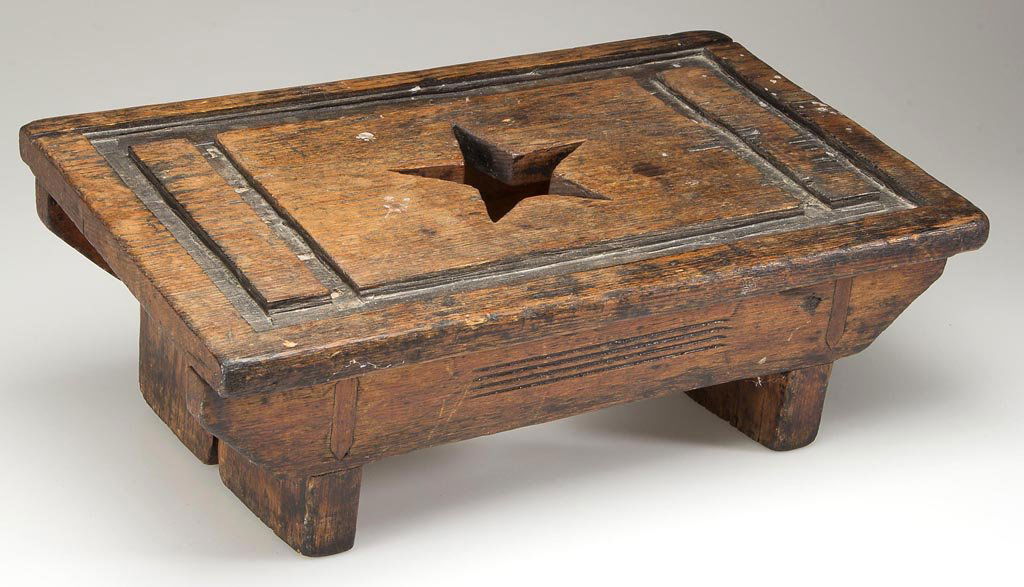 AMERICAN CARVED PINE FOOT STOOL: AMERICAN CARVED PINE FOOT STOOL, angled form with cut-out central star and carved designs. Old worn finish with remnants of old dark stain or black paint. Circa 1870-1900. 5" H, 13 1/4" W, 8" D. Prove