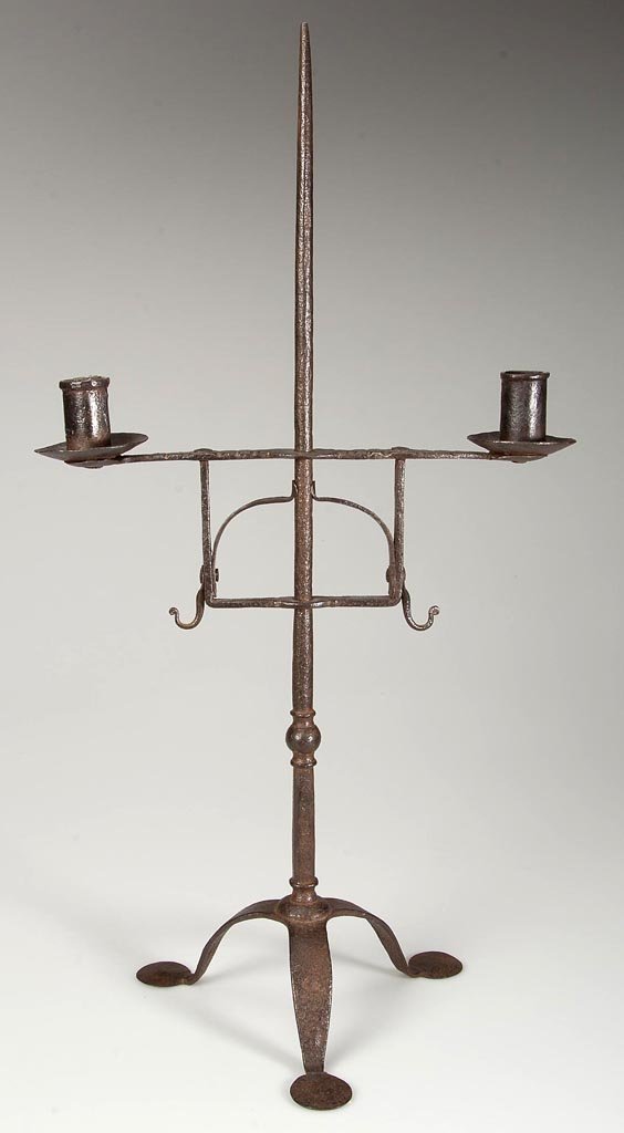 WROUGHT-IRON TABLE-TOP CANDLE STAND: WROUGHT-IRON TABLE-TOP CANDLE STAND, tapered shaft supporting an adjustable two-arm candleholder with filed decoration on cross arm, raised on a tripod base terminating in oversized penny feet. 18th c