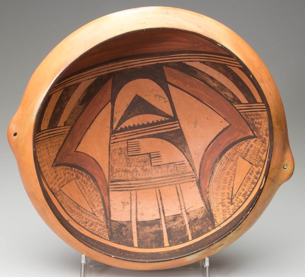 NATIVE AMERICAN HOPI POTTERY BOWL OR HANGING BASKET: NATIVE AMERICAN HOPI POTTERY BOWL OR HANGING BASKET, the low form with two flared areas punctuated by holes for hanging, the interior painted in red and black with bold geometric patterns under a thic