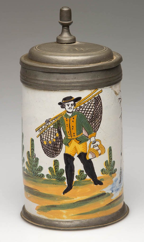 CONTINENTAL FAIENCE POTTERY TANKARD WITH PEWTER COVER: CONTINENTAL FAIENCE POTTERY TANKARD WITH PEWTER COVER AND FOOT, the body decorated with a fisherman carrying his nets by a river, painted in shades of brown, green, blue and ocher, the cover engraved