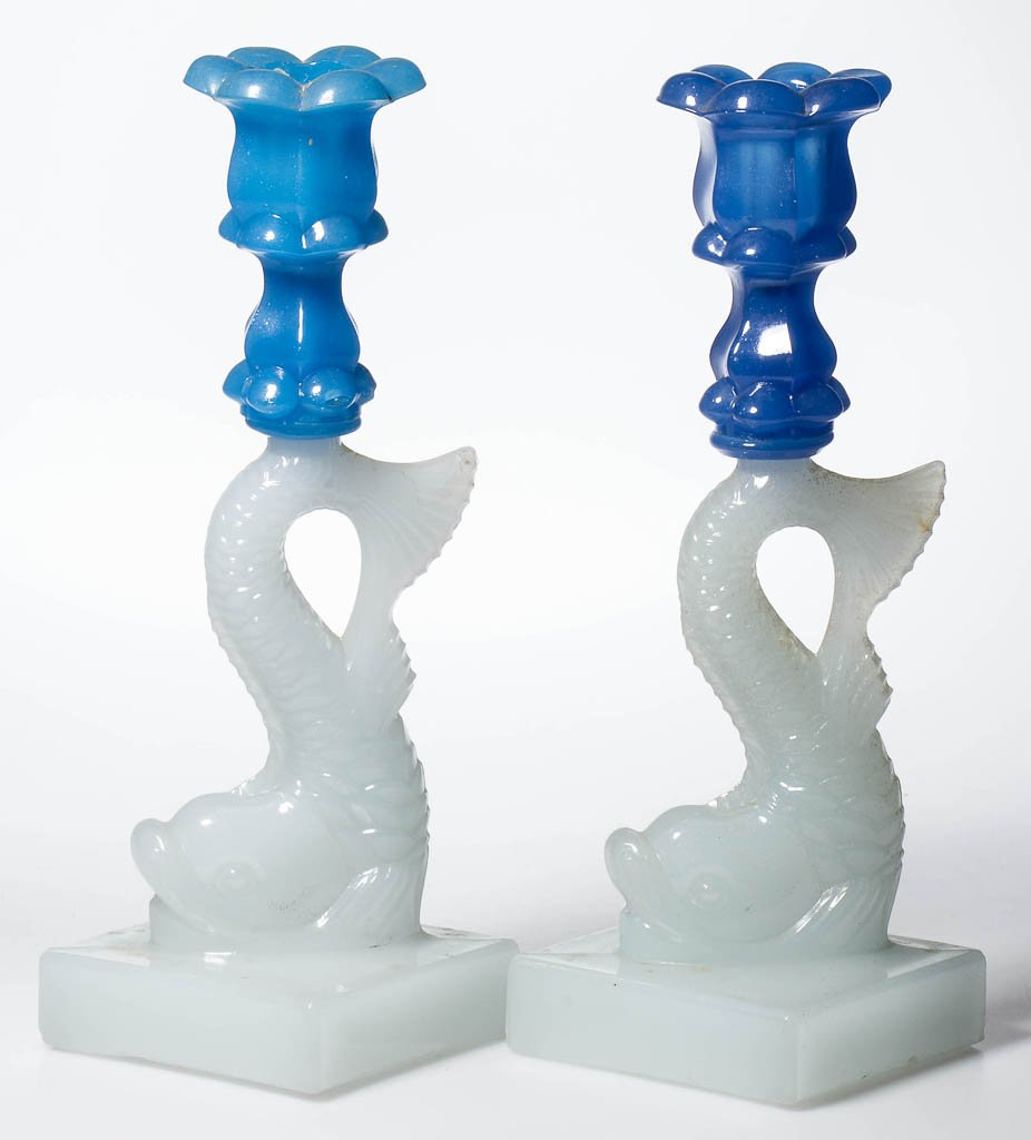 PRESSED DOLPHIN SINGLE-STEP NEAR PAIR OF CANDLESTICKS: PRESSED DOLPHIN SINGLE-STEP NEAR PAIR OF CANDLESTICKS, translucent starch blue and medium blue above alabaster/clambroth, each six-petal socket with lower extension, raised on a large dolphin-form sta