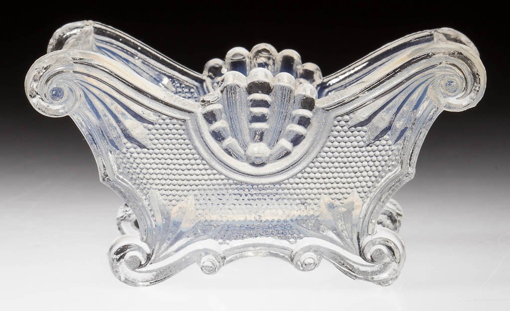 SL-14 SHELL AND HAIRPIN PRESSED OPEN SALT: SL-14 SHELL AND HAIRPIN PRESSED OPEN SALT, light opalescent, on four scroll feet. Rare. Possibly Boston & Sandwich Glass Co. Circa 1830-1845. 1 5/8" H, 2" x 3 1/8". Literature: Neal, p. 418. Provenanc