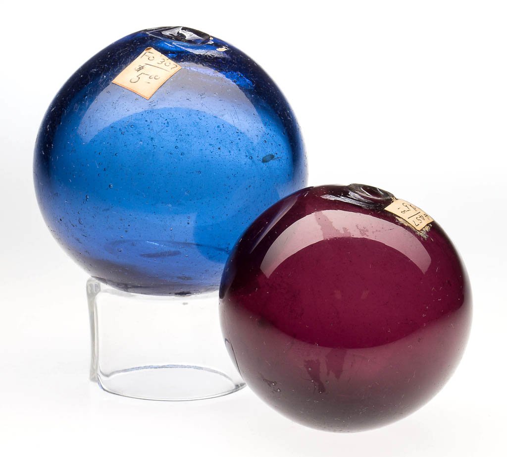 FREE-BLOWN DIMINUTIVE WITCH / COVER BALLS, LOT OF TWO: FREE-BLOWN DIMINUTIVE WITCH / COVER BALLS, LOT OF TWO, comprising an amethyst witch ball example with rough pontil having a 1/4" opening, and a medium blue cover ball with rough pontil having a 1/16" 