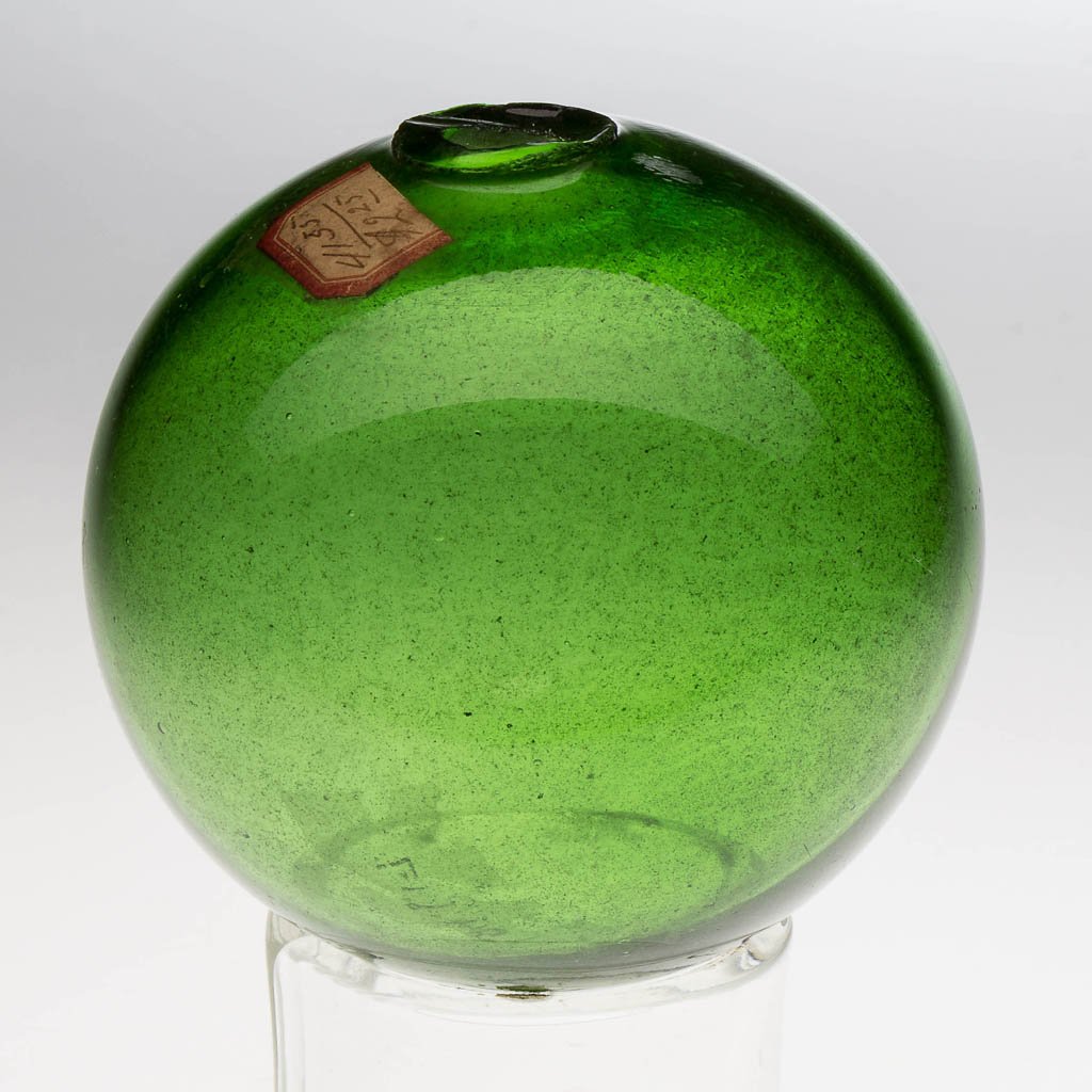 FREE-BLOWN DIMINUTIVE WITCH BALL: FREE-BLOWN DIMINUTIVE WITCH BALL, bright emerald green, rough pontil having a 7/16" opening. Probably Pittsburgh area. Circa 1850-1890. 3 1/4" D. Provenance: From the collection of the late Dr. E. R.