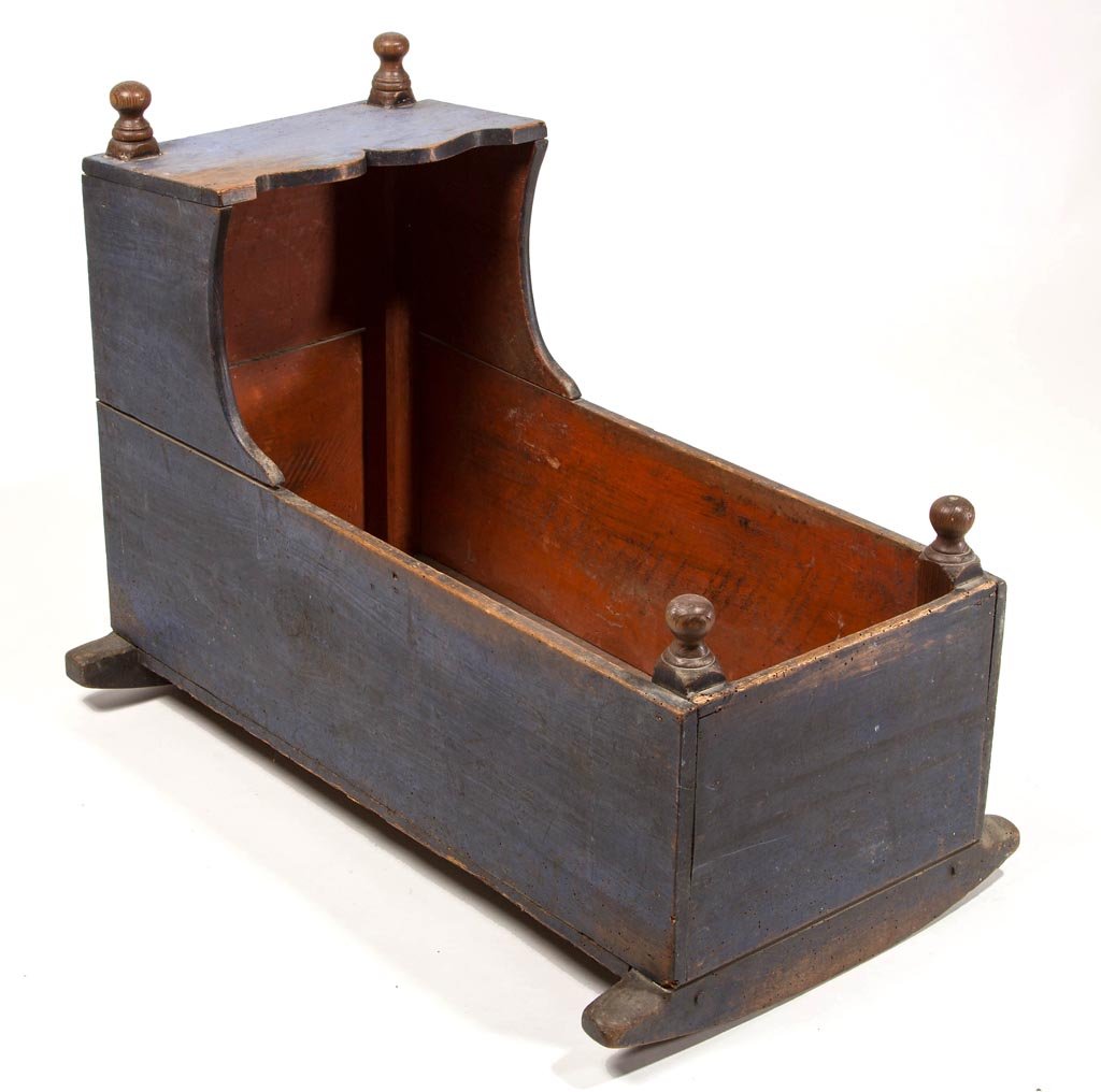 COUNTRY PAINTED PINE CRADLE: COUNTRY PAINTED PINE CRADLE, the hooded form with turned finials to square posts. Early blue- and red-painted surfaces. First half 19th century. 26 1/2" H, 34" L. Provenance: From a 35-year Augusta Co
