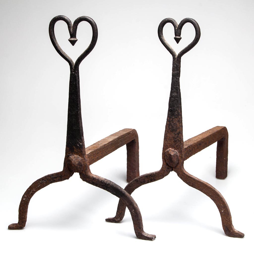 PAIR OF AMERICAN WROUGHT-IRON ANDIRONS: PAIR OF AMERICAN WROUGHT-IRON ANDIRONS, each tapered flattened shaft surmounted by a heart with pendant drop, raised on high-arched legs with slight outward projecting feet, heavy log supports riveted