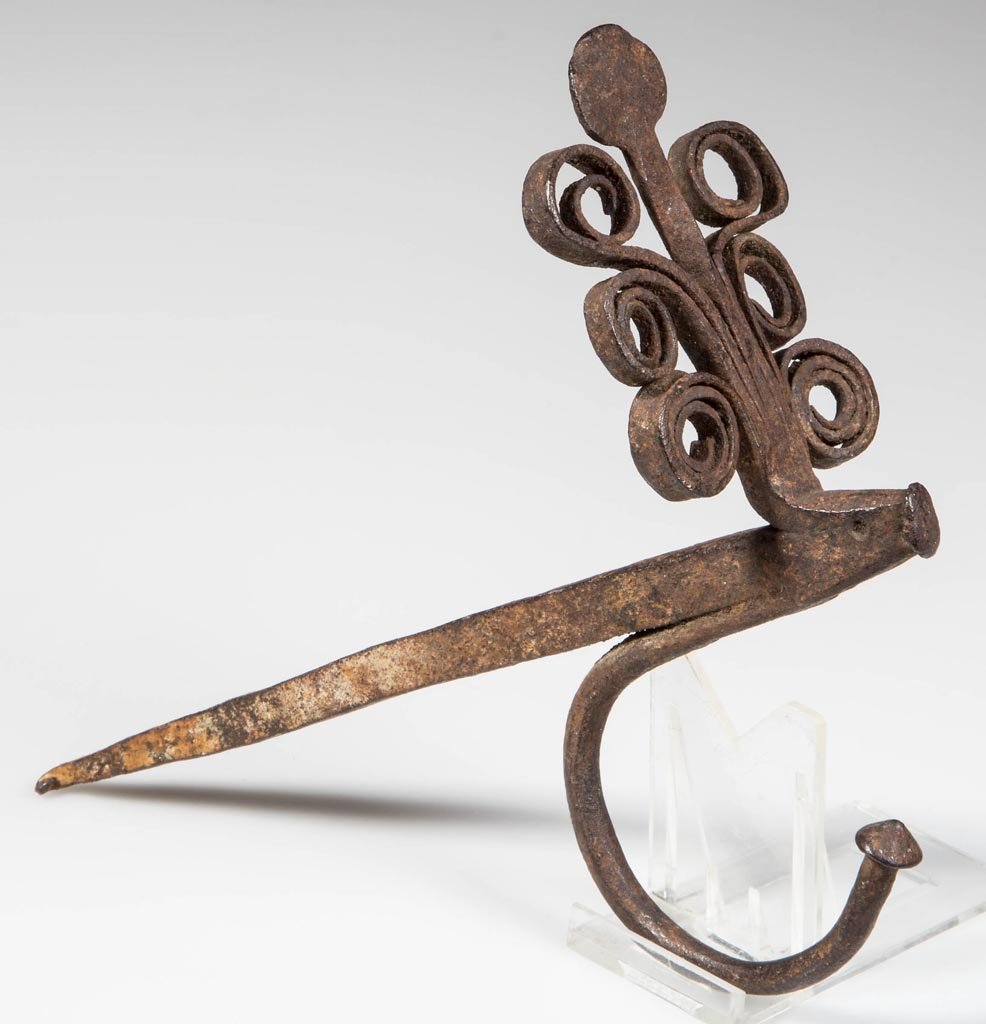 WROUGHT-IRON HORIZONTAL STICKING TOMMY / JAMB HOOK: WROUGHT-IRON HORIZONTAL STICKING TOMMY / JAMB HOOK, spike with applied top ornamentation comprising a central disk with light twist and six curled bands, underside with a c-form hook. 19th century. 6"