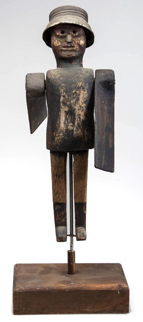 FOLK ART CARVED AND PAINTED WOOD WHIRLIGIG: FOLK ART CARVED AND PAINTED WOOD WHIRLIGIG, depicting a man wearing a tin hat fashioned from a can lid, fitted with paddle arms. Displayed on a modern wooden stand. 20th century. Figure 12" H. Provena