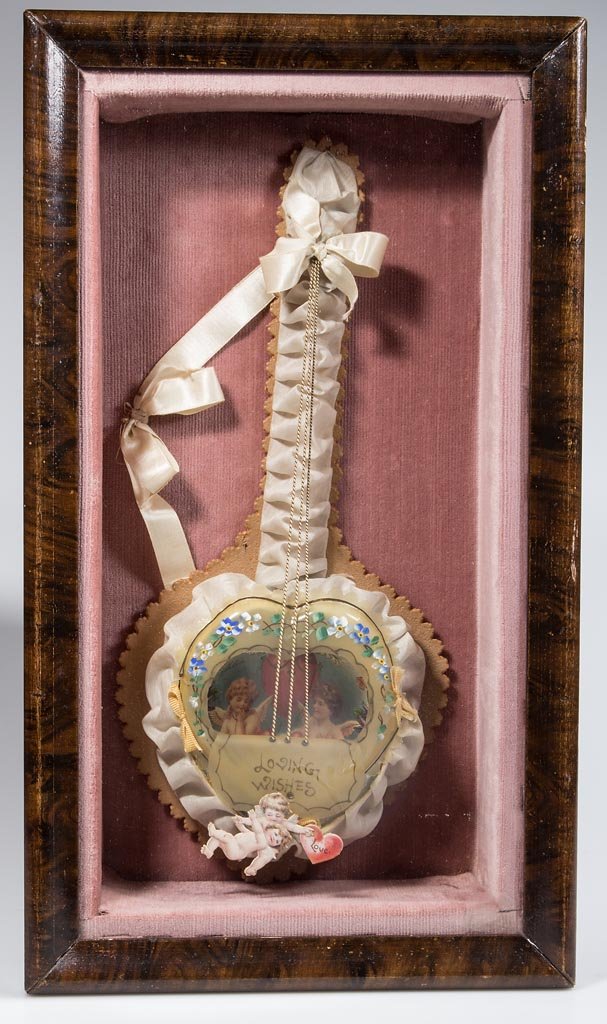 VICTORIAN FIGURAL VALENTINE: VICTORIAN FIGURAL VALENTINE, lithograph paper, celluloid, and fabric, depicting a heart-shaped banjo with three strings. Housed in a modern shadowbox frame. Probably Germany. Early 20th century. 14" L