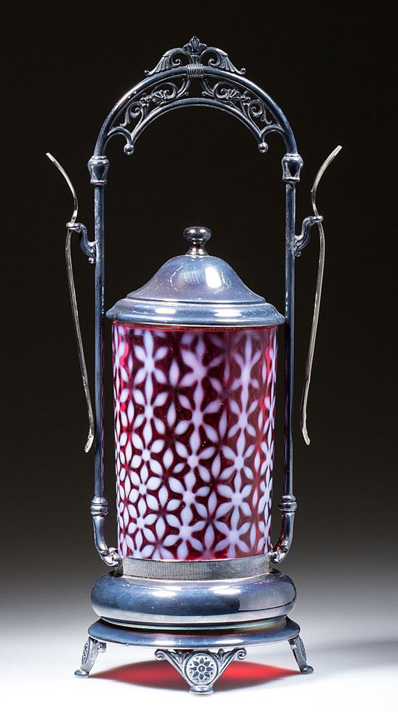 L. G. WRIGHT CHRISTMAS SNOWFLAKE PICKLE CASTER: L. G. WRIGHT CHRISTMAS SNOWFLAKE PICKLE CASTER, cranberry opalescent. Fitted in a silver-plate stand with two forks. L. G. Wright Glass Co. 20th century. Jar 5" H, 3 1/4" D. Provenance: From the colle