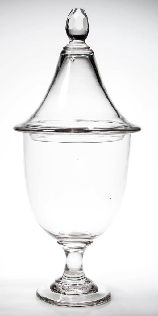 FREE-BLOWN GLASS APOTHECARY DISPLAY JAR AND COVER: FREE-BLOWN GLASS APOTHECARY DISPLAY JAR AND COVER, colorless, deep urn-form bowl raised on an applied stem and thick circular foot with polished pontil mark, peaked cover with pinched rim flange and a