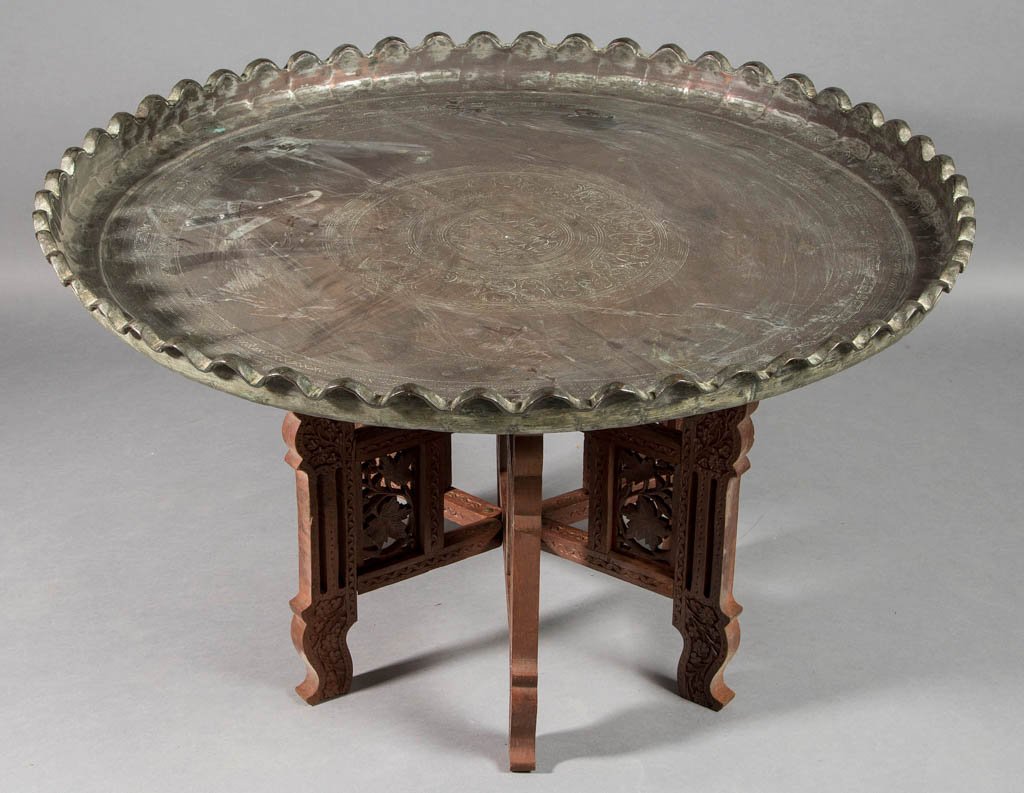 INDO-ASIAN TIN-WASHED COPPER LARGE TRAY: INDO-ASIAN TIN-WASHED COPPER LARGE TRAY, with engraved decoration and upright crimped rim, on a carved-wood, low-folding stand. Late 19th and/or 20th century. 17" HOA, 28 1/2" D. Provenance: Property 