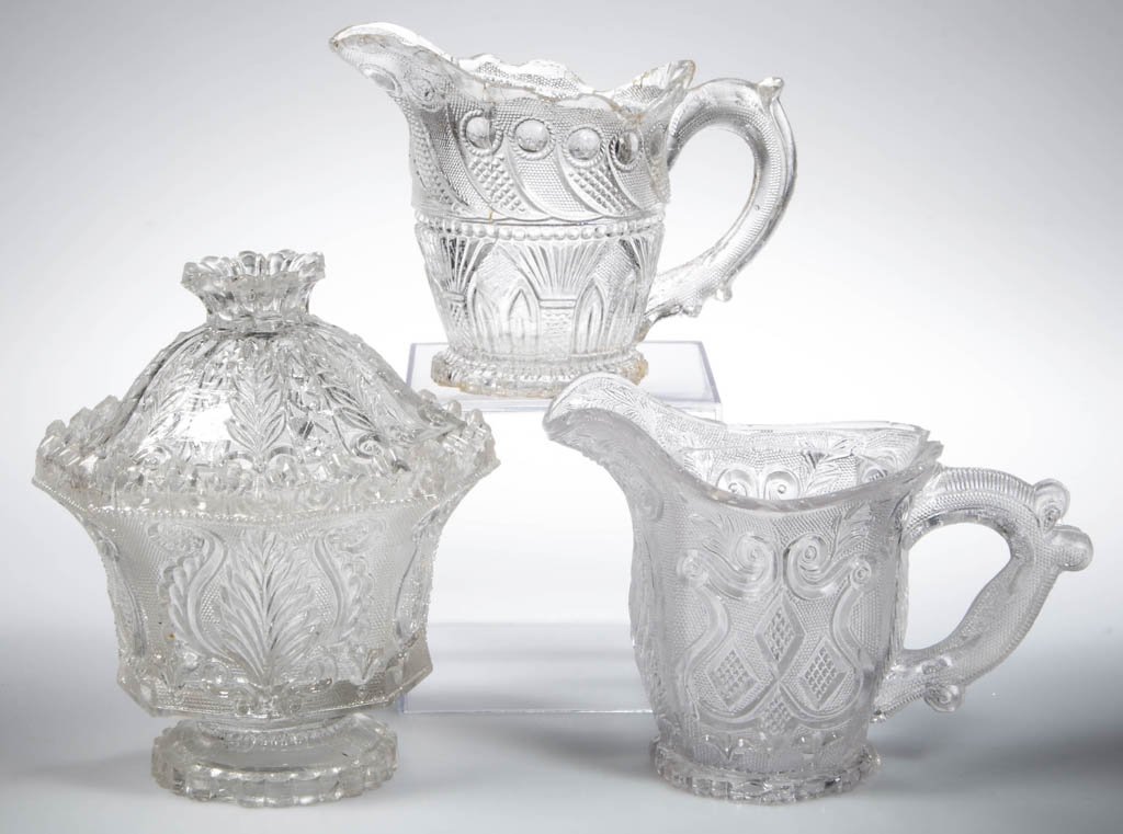 ASSORTED PRESSED LACY ARTICLES, LOT OF THREE: ASSORTED PRESSED LACY ARTICLES, LOT OF THREE, colorless, comprising an Acanthus Leaf and Shield creamer and sugar with fancy rim and correct cover, and a Peacock Eye and Gothic Arch creamer. Boston & 