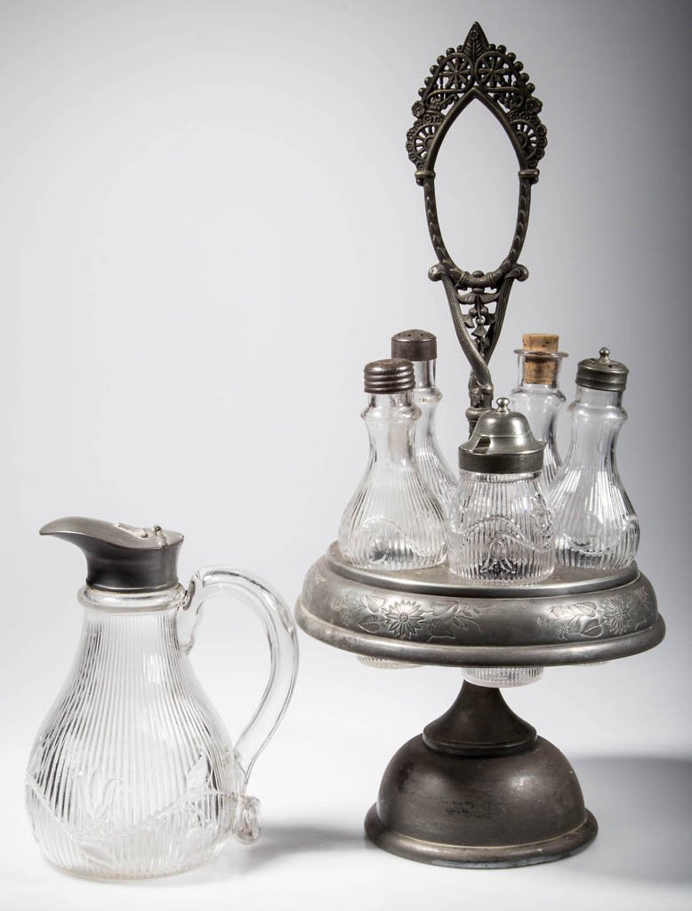 BELLFLOWER - SINGLE VINE ARTICLES, LOT OF TWO: BELLFLOWER - SINGLE VINE ARTICLES, LOT OF TWO, colorless, comprising a molasses jug with applied hollow handle, and an assembled five-bottle caster set fitted in a later quadruple-plate stand. Third q
