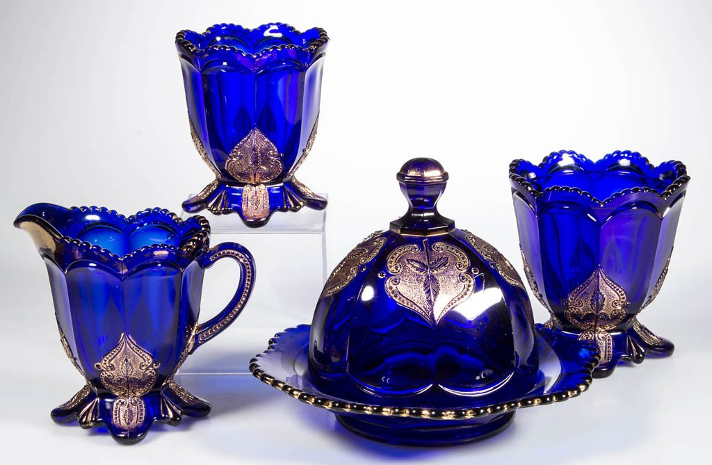 NORTHWOOD REGENT / LEAF MEDALLION FOUR-PIECE TABLE SET: NORTHWOOD REGENT / LEAF MEDALLION FOUR-PIECE TABLE SET, cobalt blue with gilt decoration, comprising a butter dish, creamer, spooner, and sugar lacking cover. Northwood Glass Co. Late 19th/early 20th