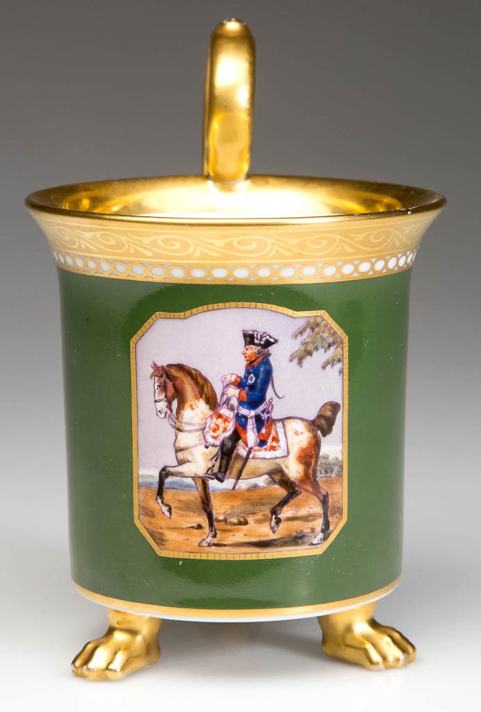 GERMAN KPM PORCELAIN CABINET CUP ON FEET: GERMAN KPM PORCELAIN CABINET CUP ON FEET, cylindrical, with flaring rim, on three gilt paw feet, the acanthus-stem handle with flower head resting on rim, painted with a dark green band under patterne