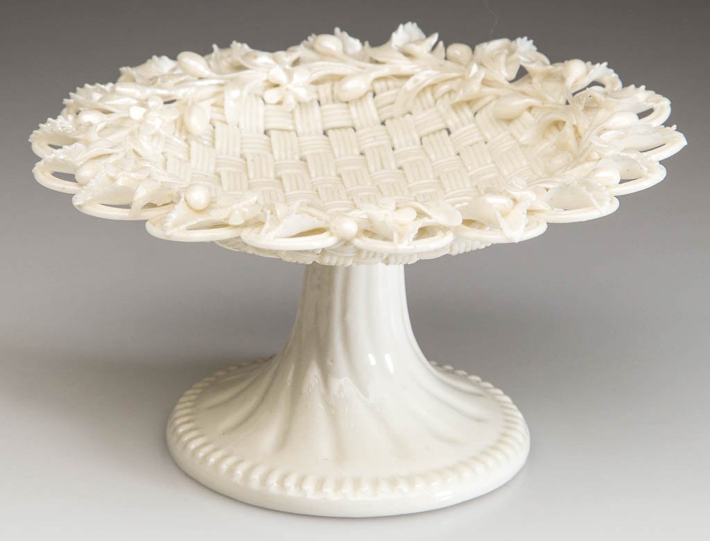 IRISH BELLEEK PORCELAIN RING STAND: IRISH BELLEEK PORCELAIN RING STAND, formed as a miniature footed basket, the four-strand basket weave with loops to the edge, with a floral garland applied to the top, on a beaded pedestal base. Secon