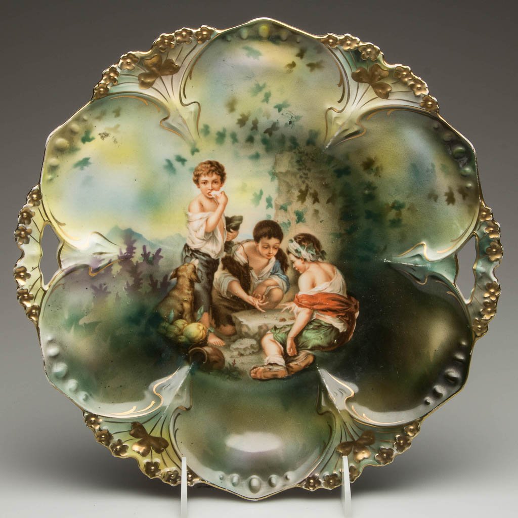 GERMAN R.S. PRUSSIA PORCELAIN DICE THROWERS CAKE PLATE: GERMAN R.S. PRUSSIA PORCELAIN DICE THROWERS CAKE PLATE, shaped and molded large, shallow bowl, in mold #82, printed with Murillo "Dice Thrower" to center, wreath, star and printed marks to underside. 
