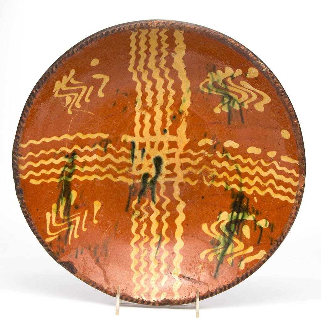 PENNSYLVANIA SLIP-DECORATED EARTHENWARE / REDWARE: PENNSYLVANIA SLIP-DECORATED EARTHENWARE / REDWARE CHARGER, lead-glazed, semi-deep form with coggled rim, center with strong yellow-slipped decoration and copper splashes. Second half 18th century. 2 3
