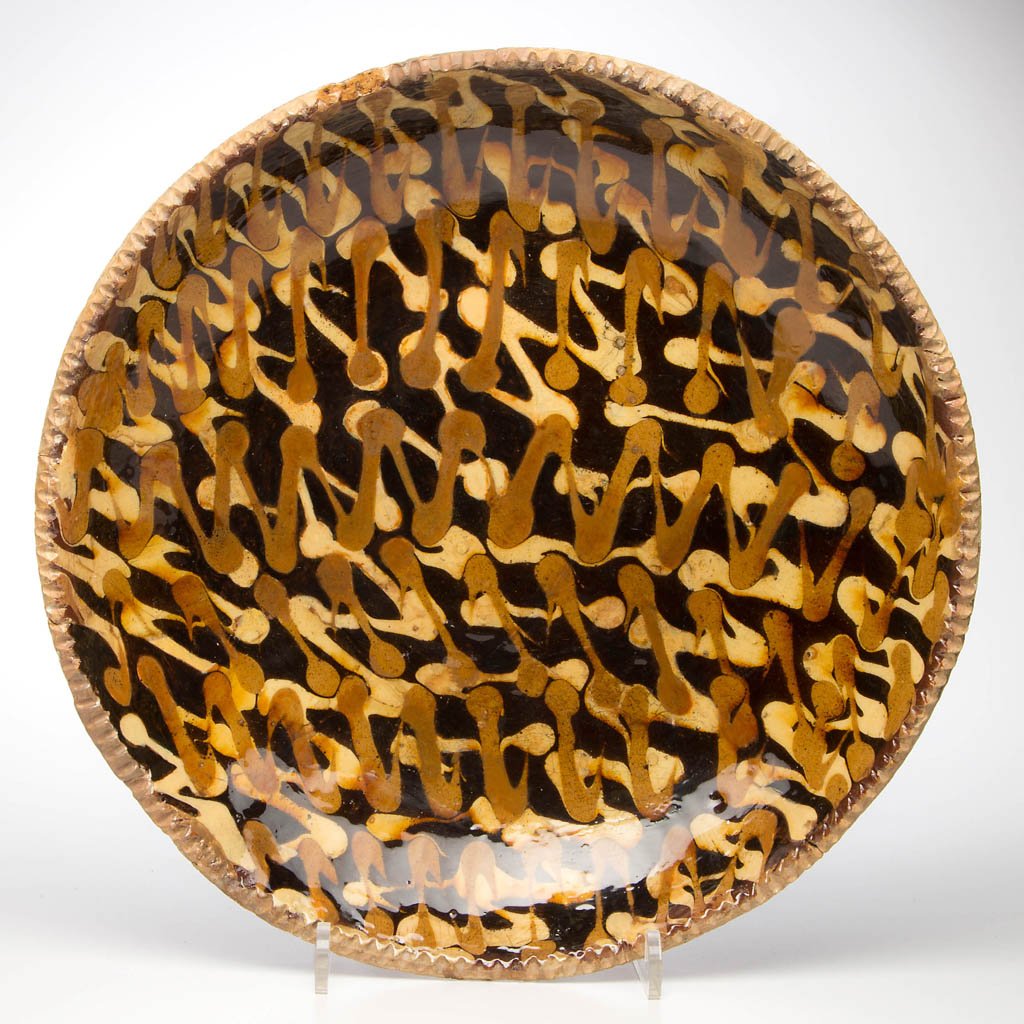 SLIP-DECORATED EARTHENWARE / REDWARE CHARGER: SLIP-DECORATED EARTHENWARE / REDWARE CHARGER, lead-glazed, shallow form with coggled rim, center with brown- and yellow-slipped decoration over a manganese wash. Second half 18th century. 2 1/4" H, 13