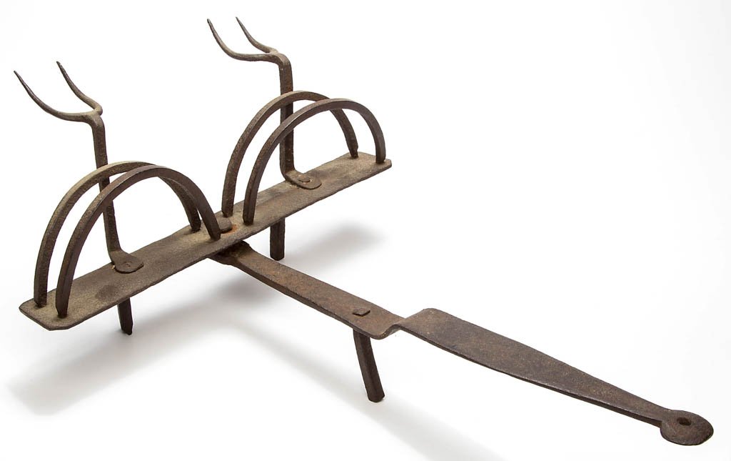 WROUGHT-IRON HEARTH TOASTER: WROUGHT-IRON HEARTH TOASTER, central shaft riveted to a revolving rack with a pair of double arches and two flesh forks, supported by three simple feet, handle terminating in a disk form. 18th or earl