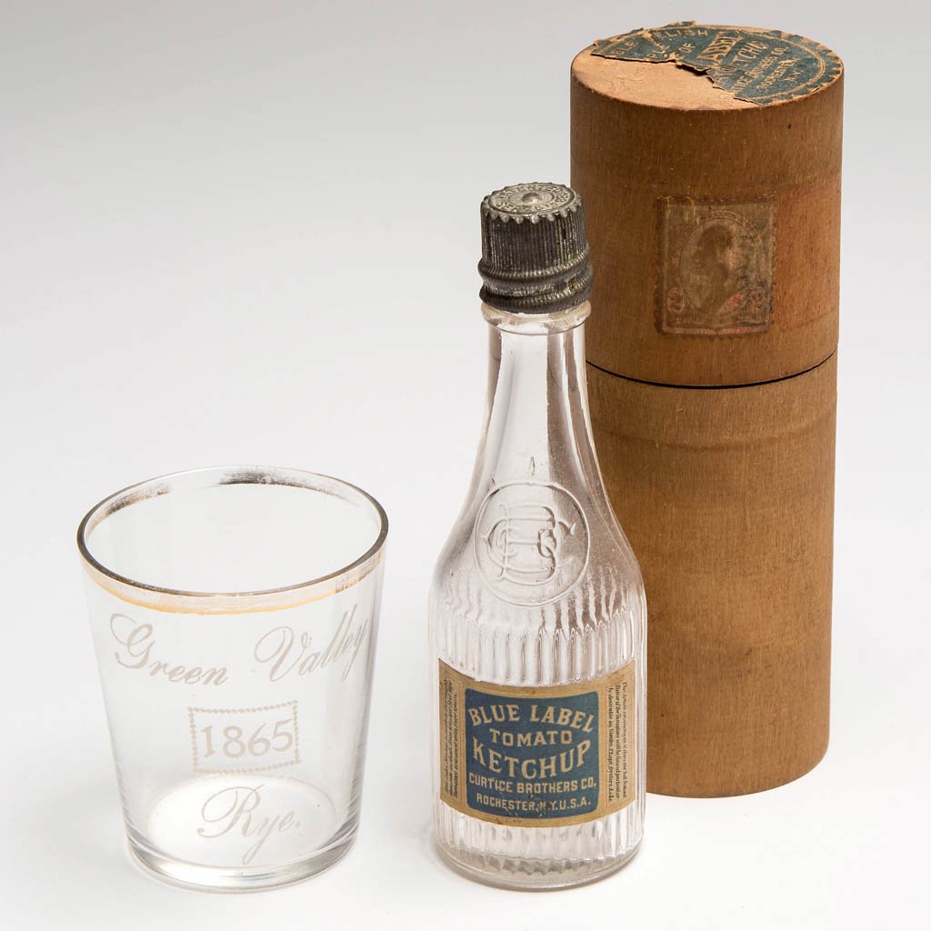 ASSORTED GLASS ADVERTISING ARTICLES, LOT OF TWO: ASSORTED GLASS ADVERTISING ARTICLES, LOT OF TWO, comprising a Blue Label Tomato Ketchup sample bottle with original label, screw cap, and wooden shipping container, and a "Green Valley 1865 Rye" whisk